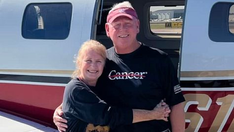 Woman hugs a man wearing a shirt with the word, cancer, and red line strikethrough.