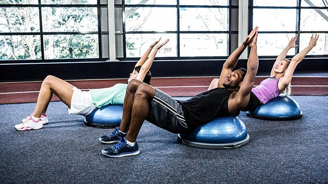 Three people work out with BOSU balls at a gym class.