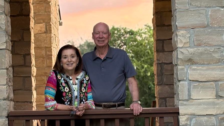 A woman and man stand side-by-side with a sunset in the background