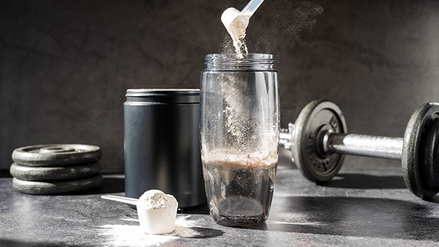creatine powder being poured into a shaker bottle next to a barbell