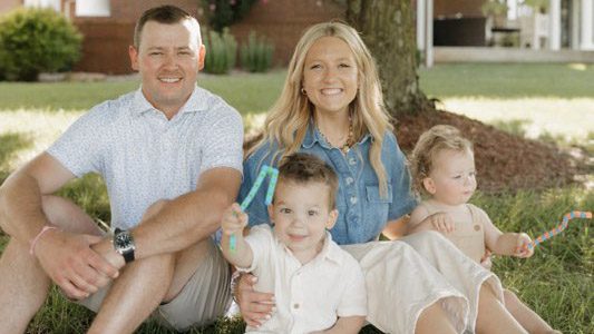 A man and a woman sit in the grass with two baby boys