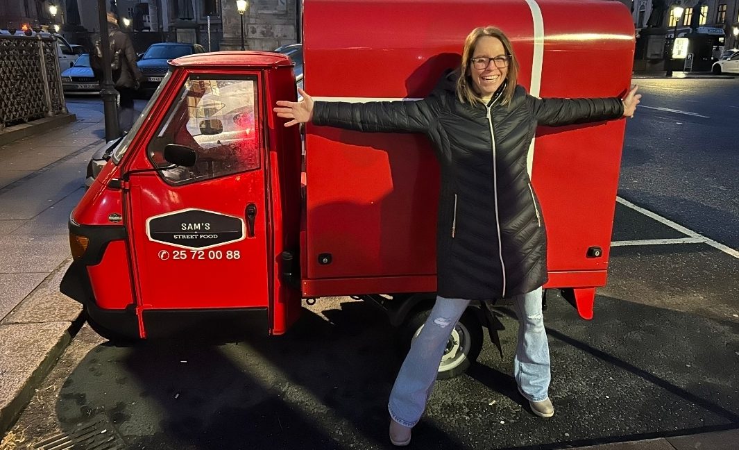 Woman stands in front of a red car with her arms wide open