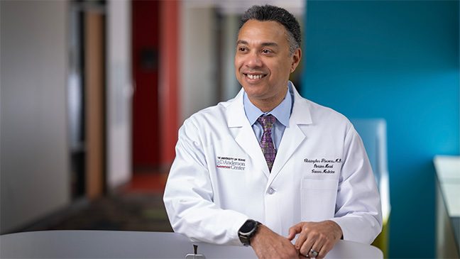 Smiling man in white coat, blue shirt and purple tie in a clinic.