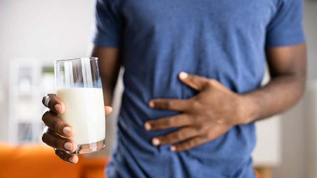 Black man holds stomach with one hand and a glass of milk in the other