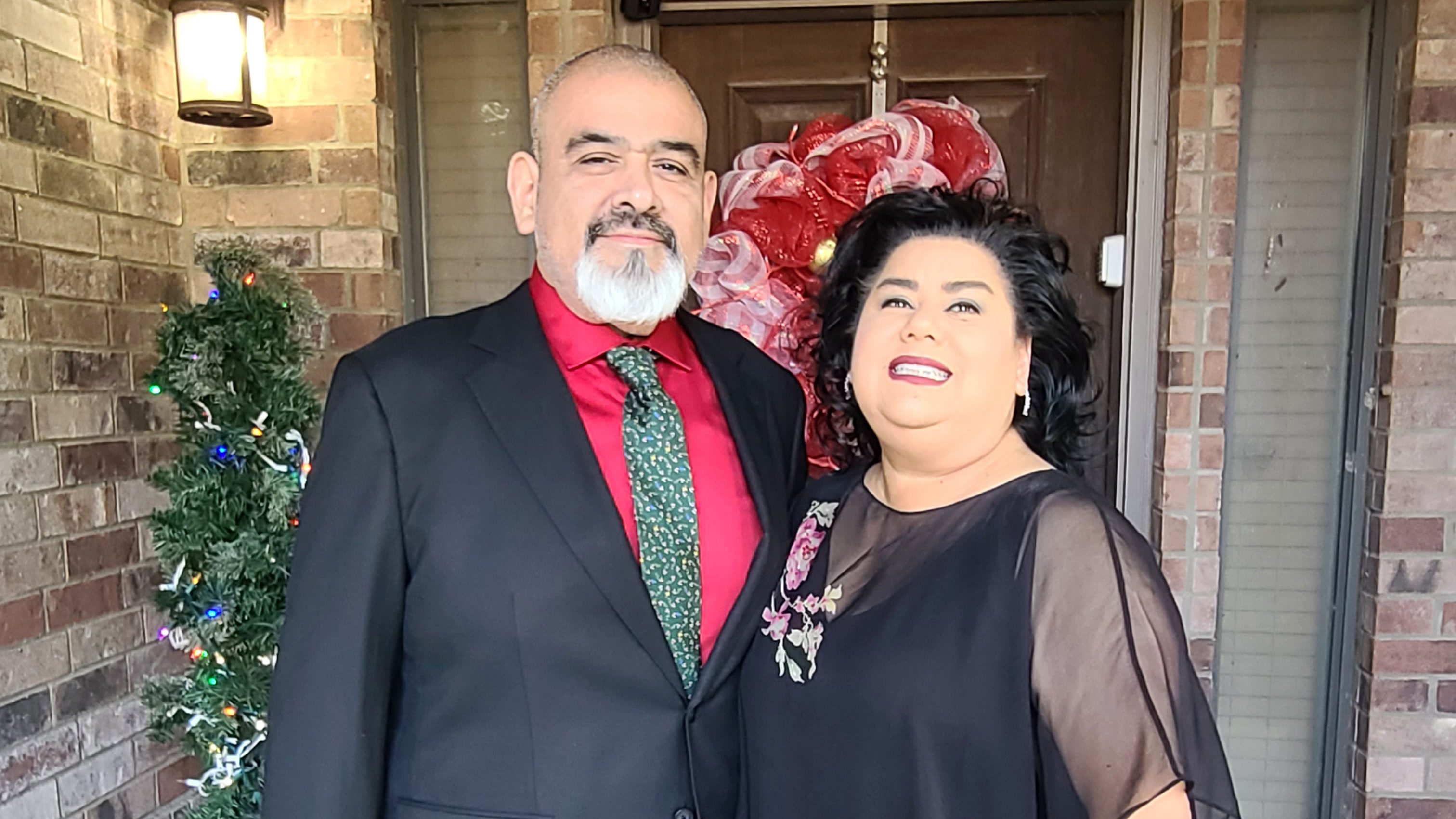 A man and woman stand in front of a door decorated for the holidays