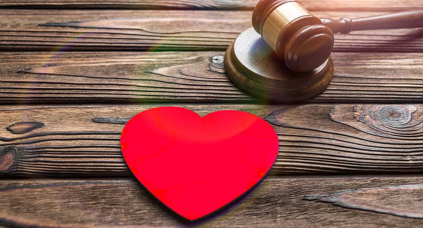 Bright red paper heart next to a judge's gavel on a rustic wooden tabletop