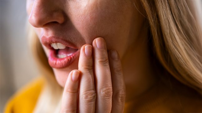Woman holds the side of her mouth in pain