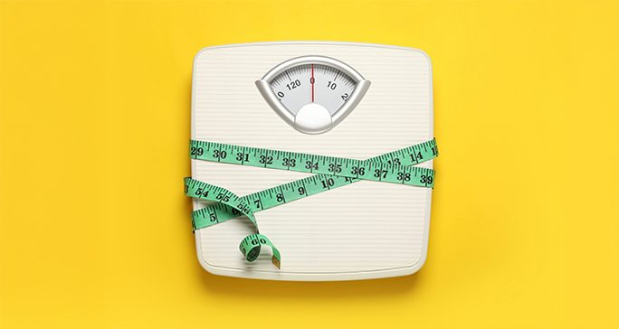 White scale wrapped with a green measuring tape against a yellow background.