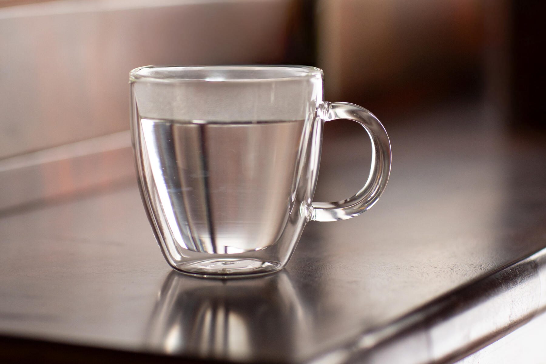 clear mug of hot water sitting on a desk, benefits of drinking hot water