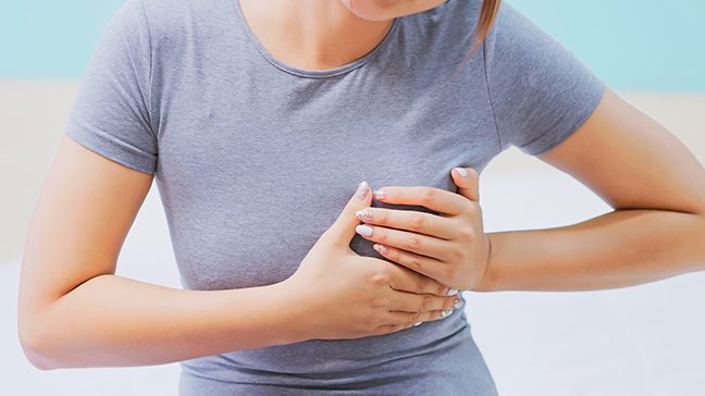 Young woman wearing a grey T-shirt holds her hands on her left breast.