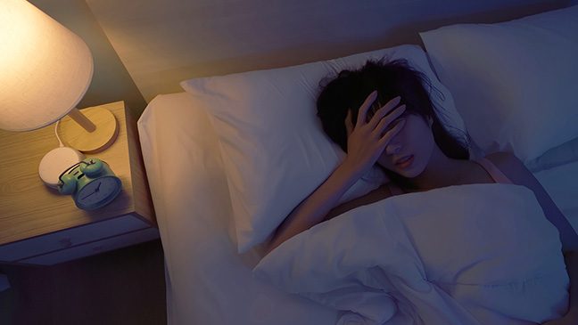 Woman lying in bed with a hand over her head