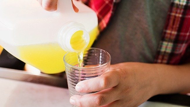 Person in plaid shirt pours a gallon of yellow liquid into a clear glass