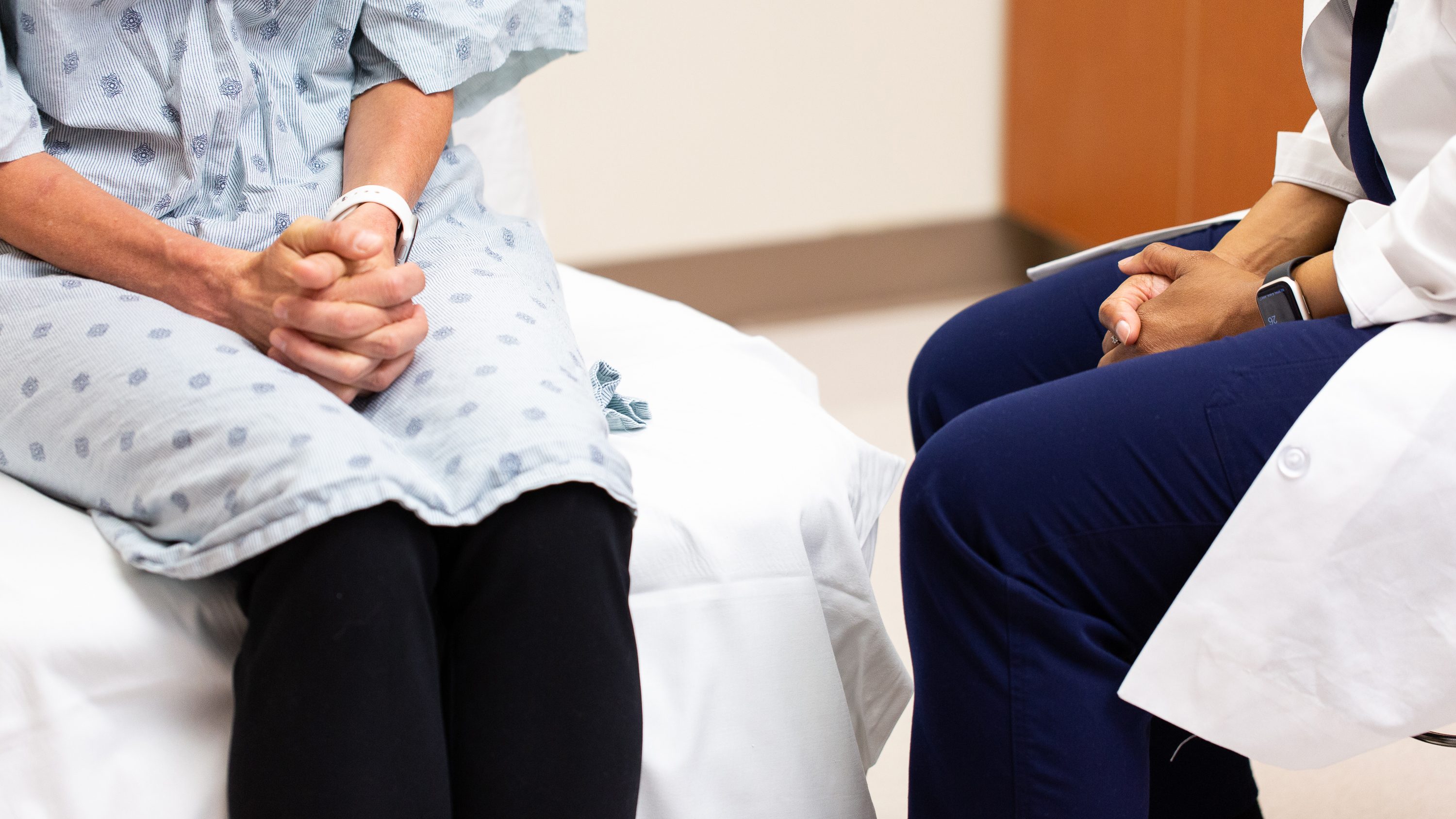 A doctor and a patient's knees and hands can be seen as they sit facing each other