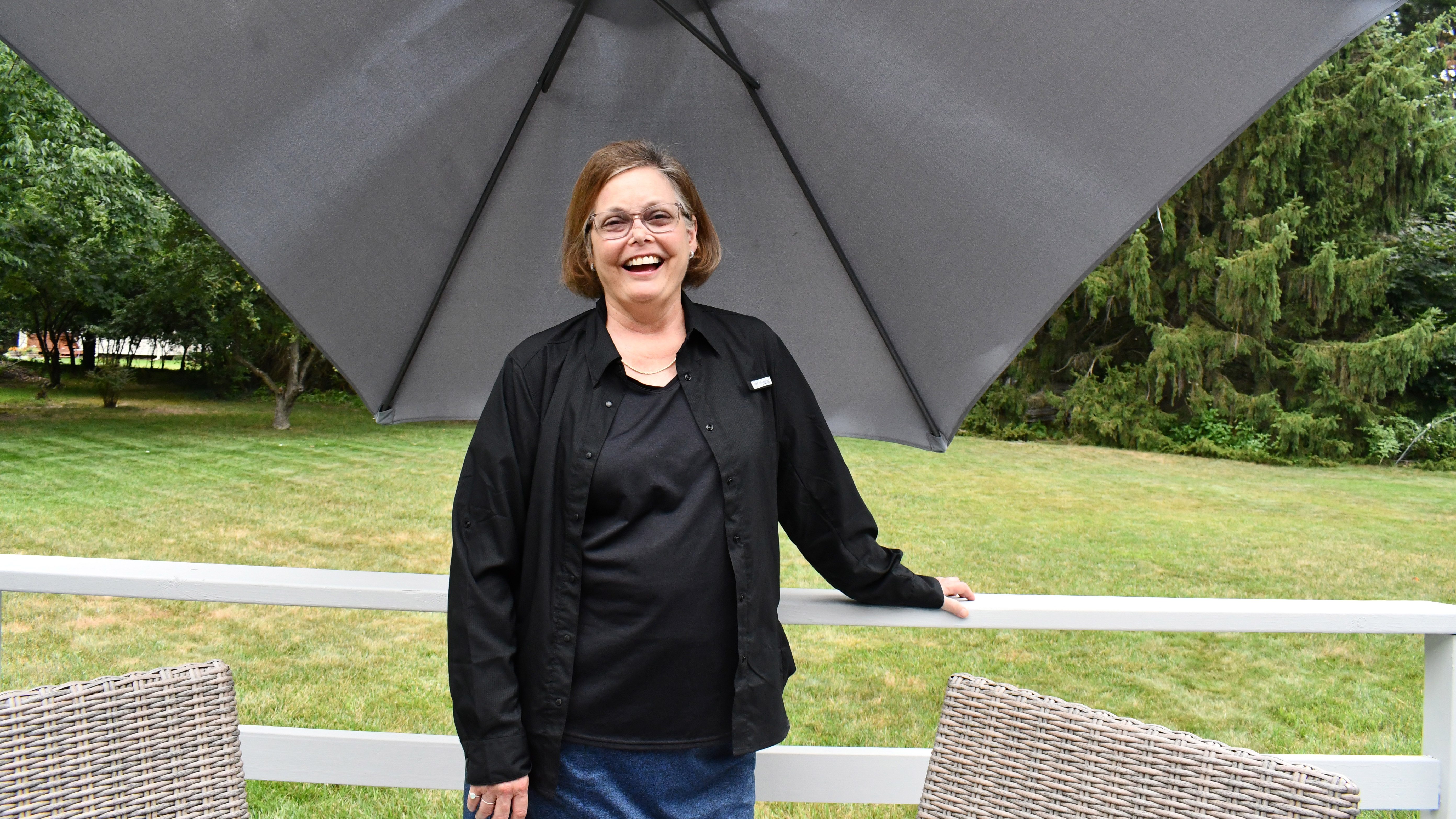 Woman wearing all black stands outside under a large shade umbrella