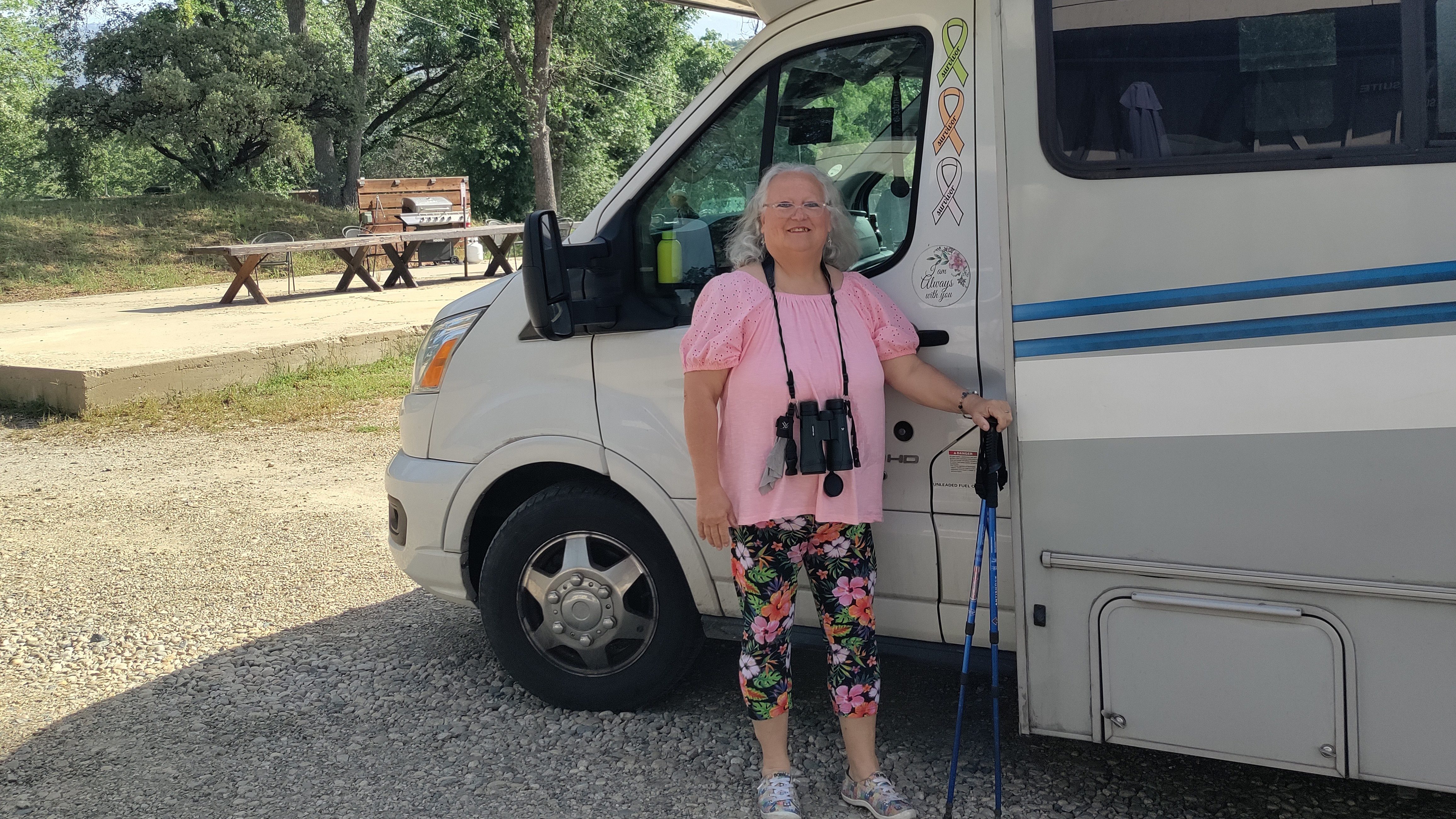 Woman with binoculars around her neck stands next to an RV. 