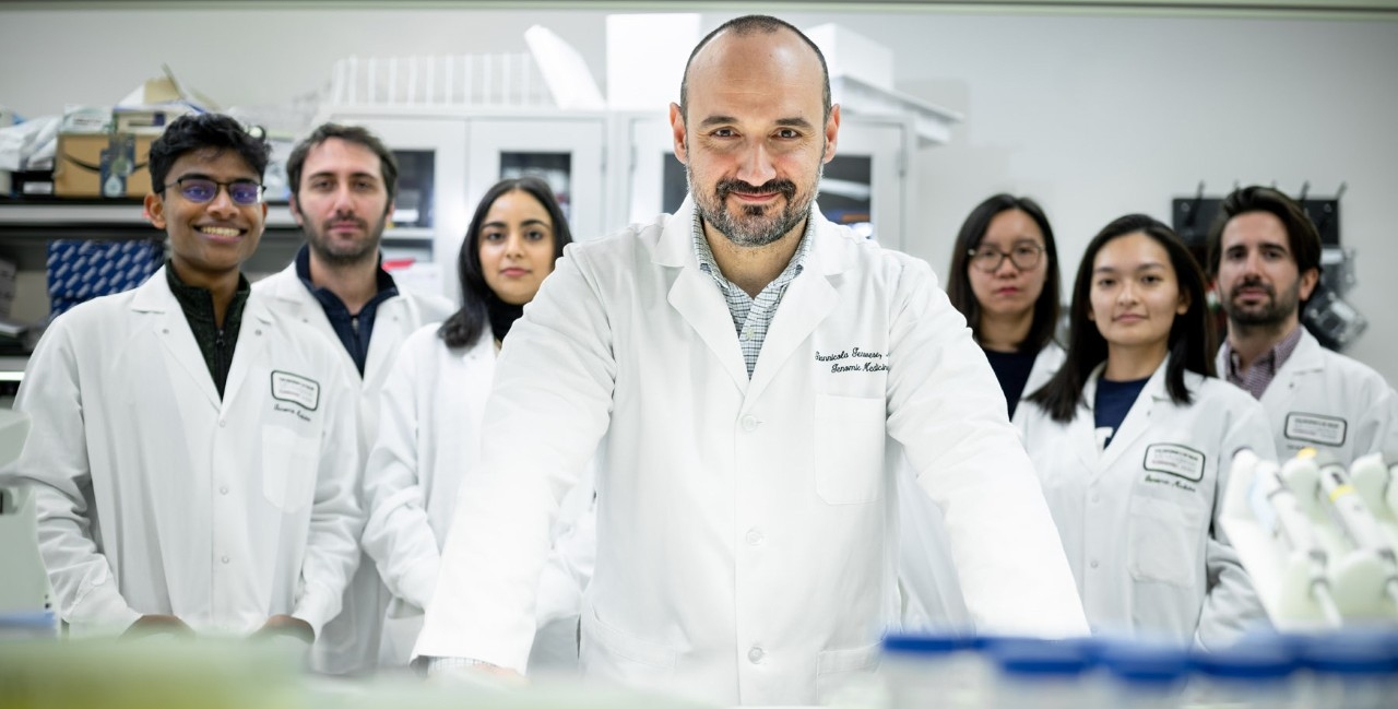 Man in white lab coat stands in the foreground with six people in matching white coats standing behind him