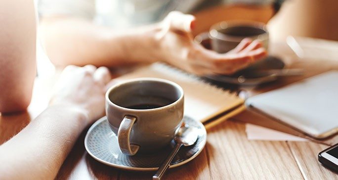 Close-up of two people's hands gesturing on a table with coffee cups