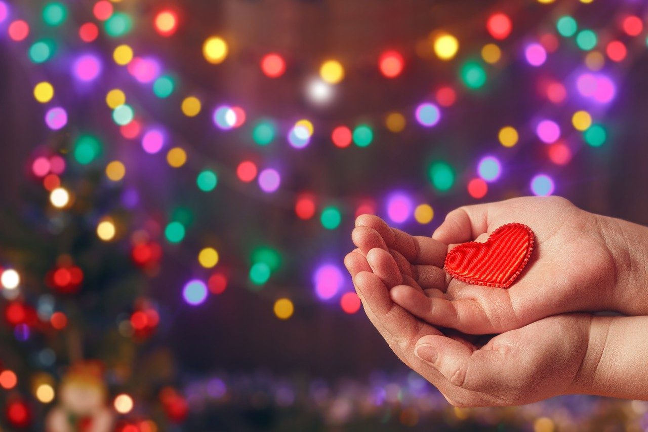 Hands holding a felt heart by holiday lights