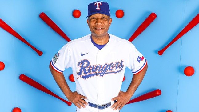 Texas Rangers coach Tony Beasley smiles at camera, before baseball-themed backdrop