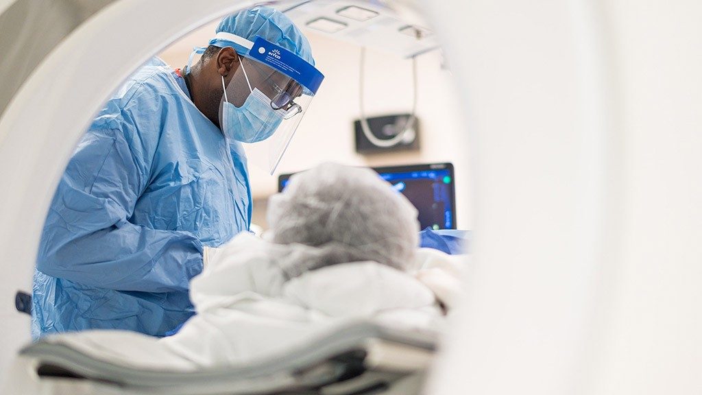 Stephen McRae, M.D., performs surgery in the operatinh room while wearing a face mask and face shield.