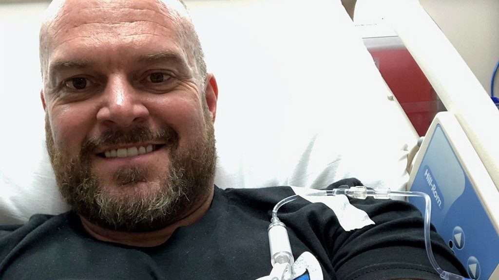 Stage IV melanoma survivor Bradley Evans, Psy.D., smiles as he sits in his hospital bed