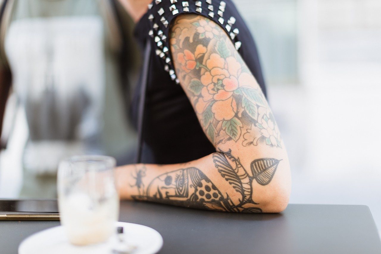 Woman with tattooed arm sitting at a table with coffee
