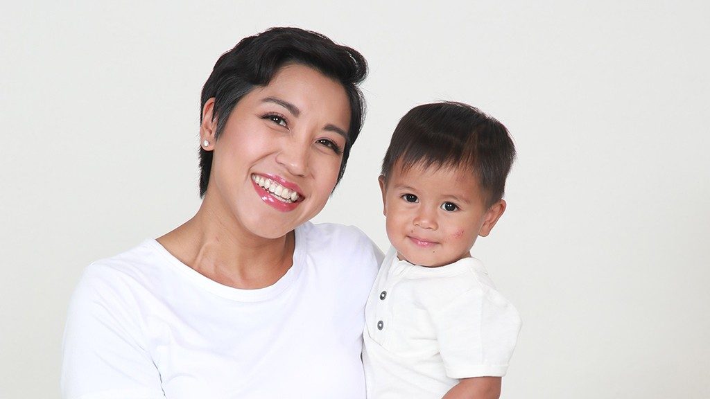 Breast cancer survivor Gretchen Lee Herrera bolds her son, Liam. Both have short black hair and are wearing white against a white background.