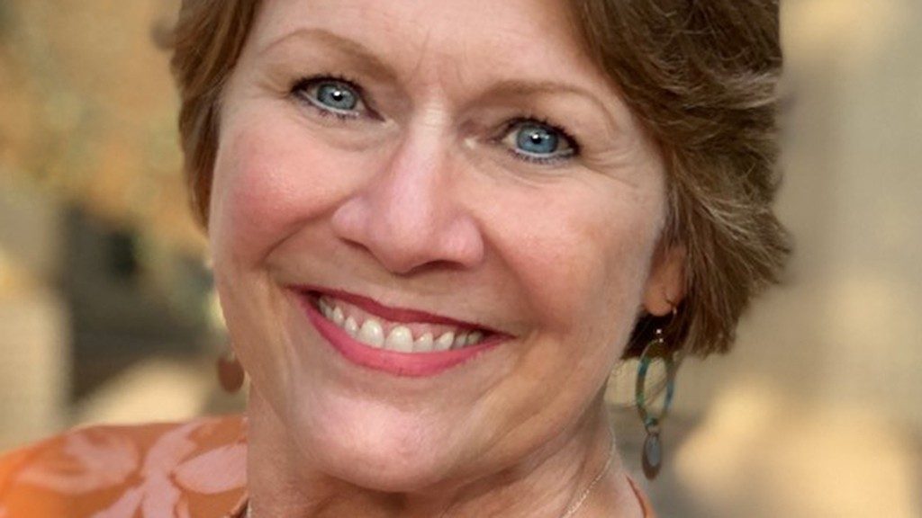 Close-up photo of bladder cancer survivor Margo Wickersham, smiling. She has short hair, earrings and blue eyes.