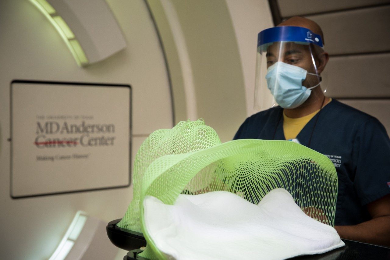 Kristoffer Semien, radiation therapy clinical supervisor, holds a radiation therapy mask used to treat head and neck cancer patients while he wears a medical-grade face mask and face shield.