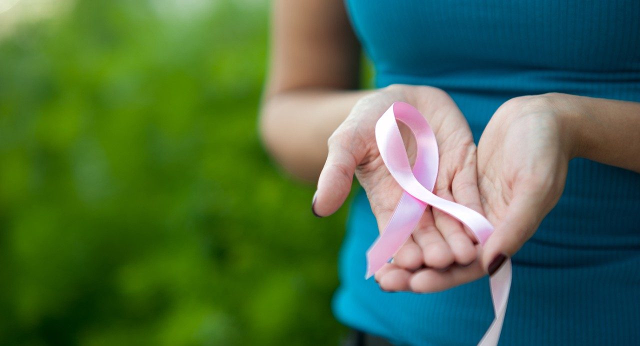 Woman is shown holding a pink ribbon photos for breast cancer awareness.