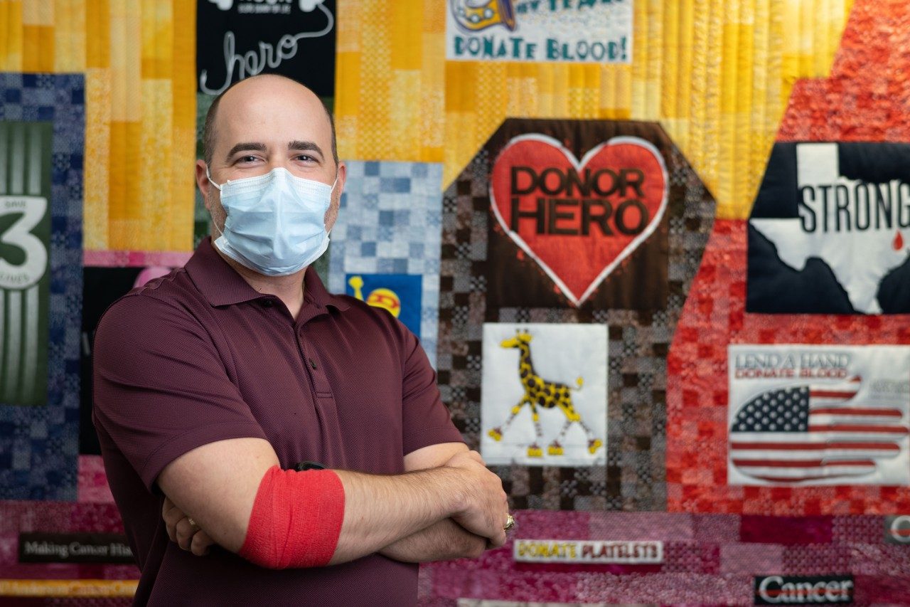 Ross Robinson standing in front of a blood donor quilt at MD Anderson Blood Bank after donating blood.
