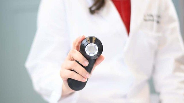 Waist-level view of doctor's outstretched hand holding a dermoscope