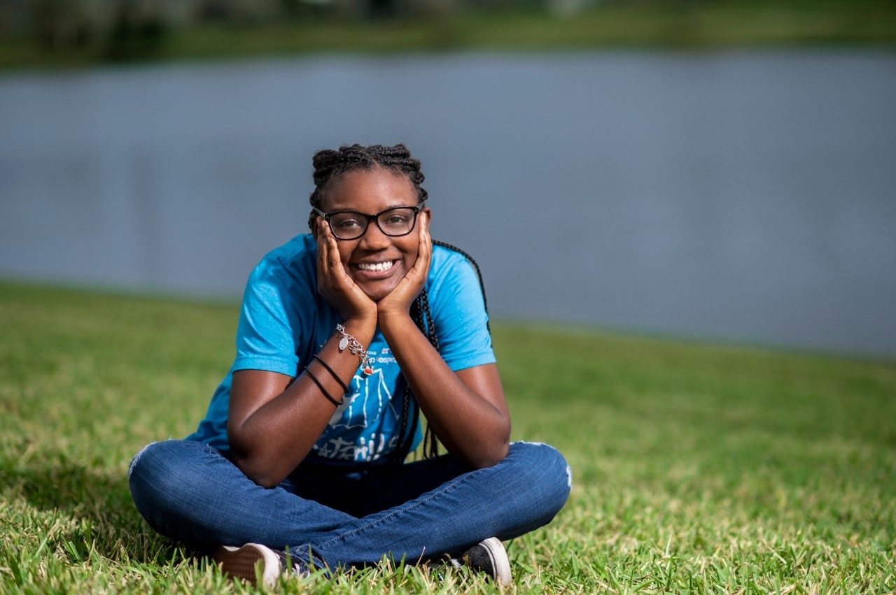 Childhood leukemia survivor Akilah Lopez sits on the grass with her hands on her chin