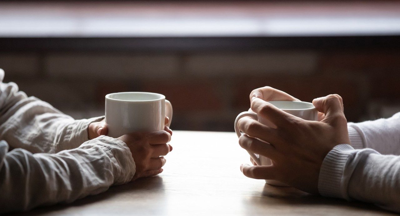 stock photo of two sets of hands cradling coffee mugs on a table, across from each other