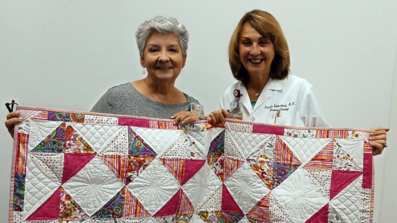 Breast cancer survivor Wendy Salinas Brouwer presents Pamela Schlembach, M.D., with one of the quilts she made.