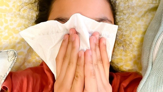 Person using both hands to cover their face with a tissue