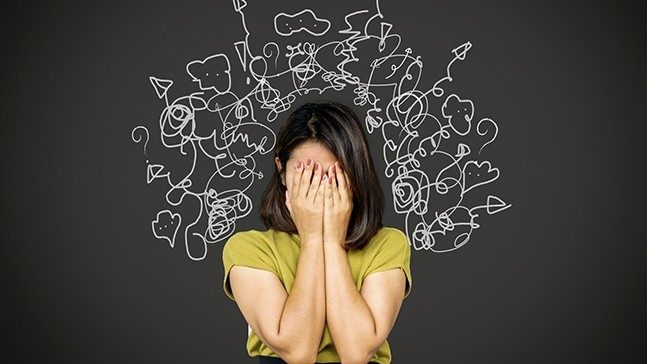 Women in green shirt holds her face in her hands. Doodles of white arrows, speech bubbles and question marks are frame her head.
