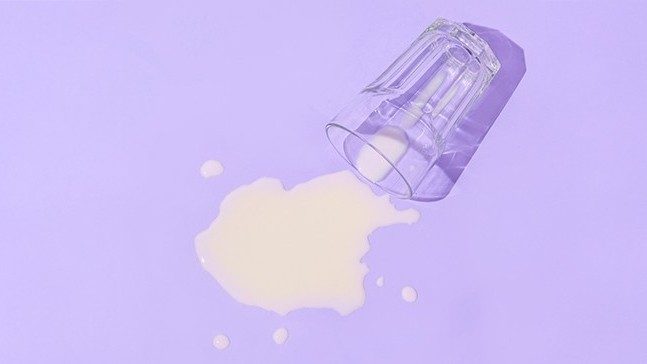 A glass of spilled milk against a purple background.