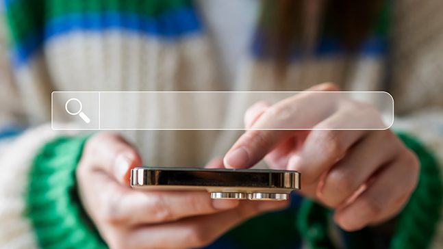 Hands holding a gold phone with an image of a search bar overlaying the image.