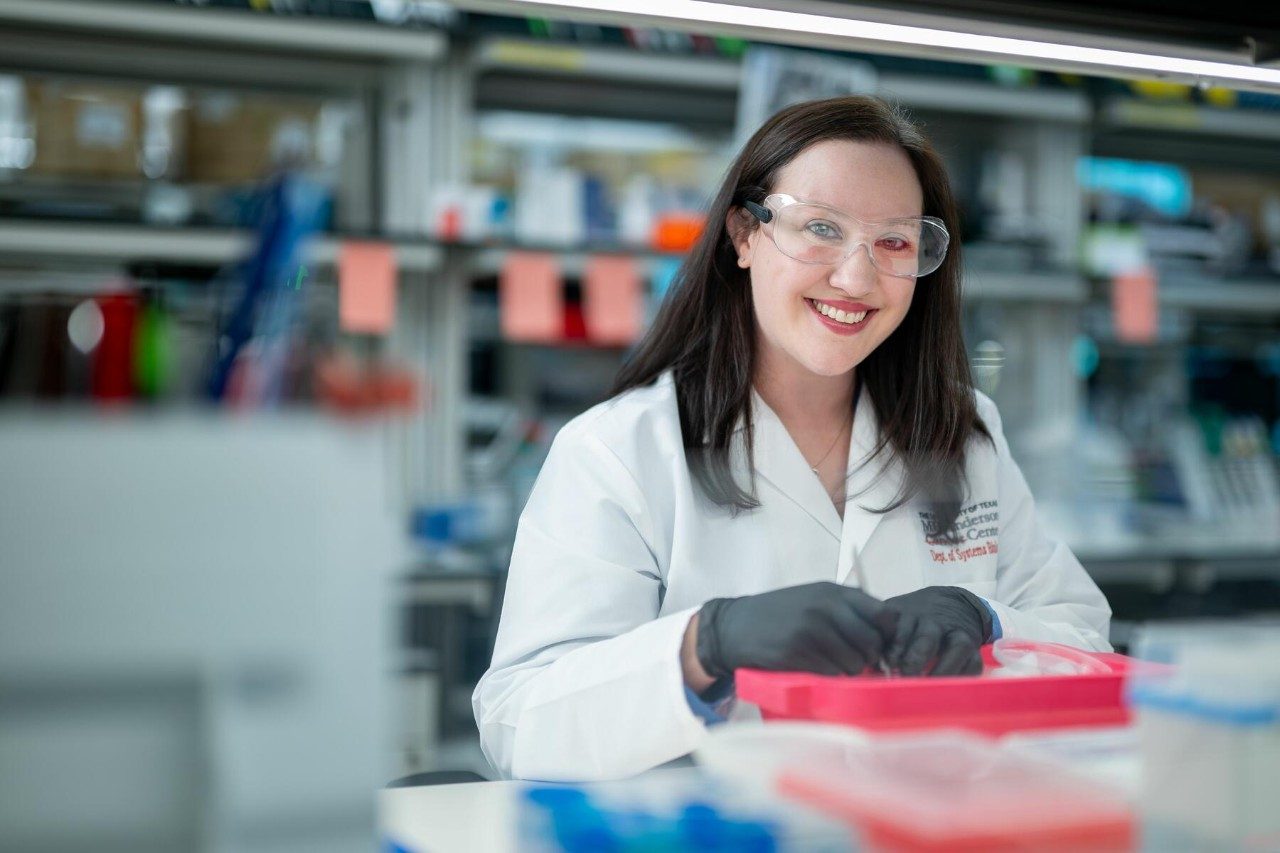 Woman with dark hair wearing a white lab coat and gray gloves works in a lab