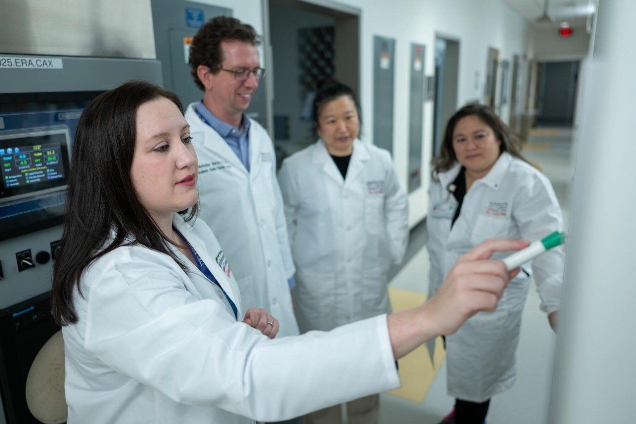Four adults wearing white lab coats standing in a hallway
