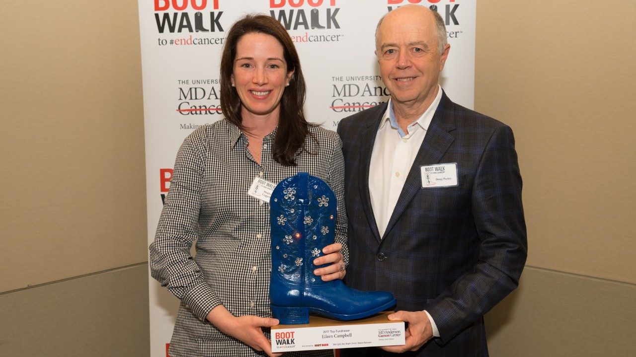 Doug Perley and Meghan Leggett hold a blue cowboy boot in front of a Boot Walk sign.