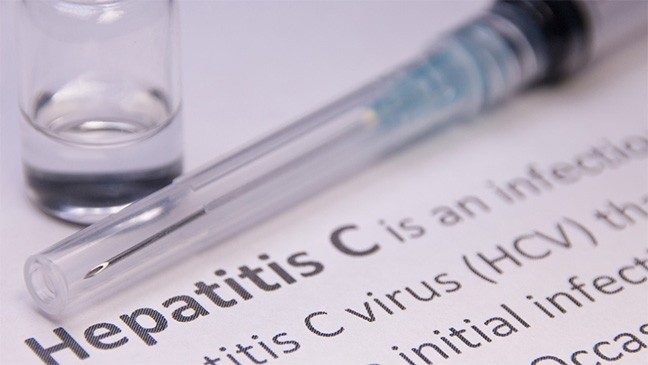 A vial of vaccine and a syringe sit on top of paperwork with information on hepatitis C 
