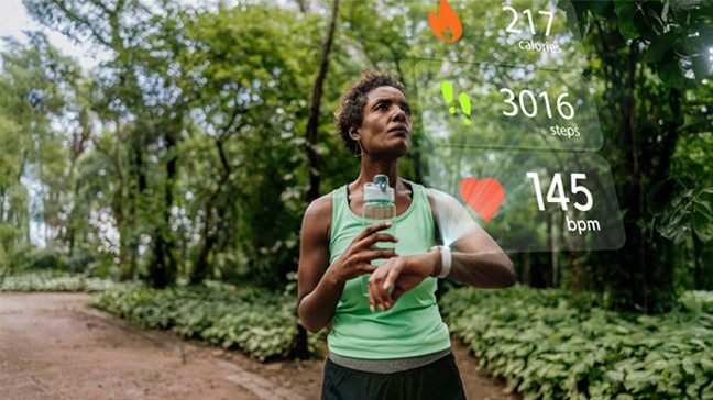 A woman in exercise gear looks at caloric burn, step count and heart rate information projected from her fitness device