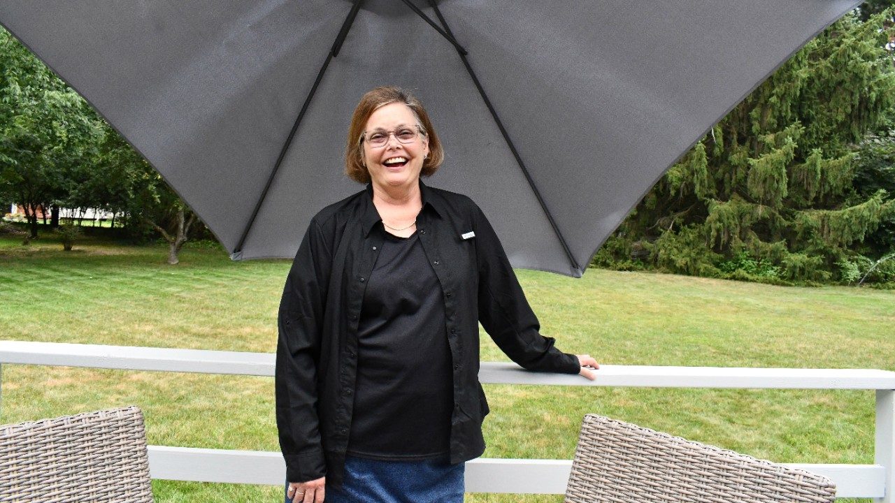 Woman wearing all black stands outside under a large shade umbrella