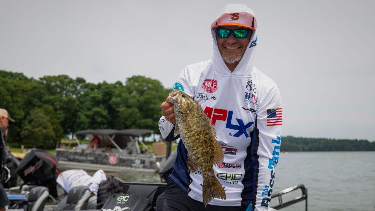 Man stands in a fishing boat holding a smallmouth bass.