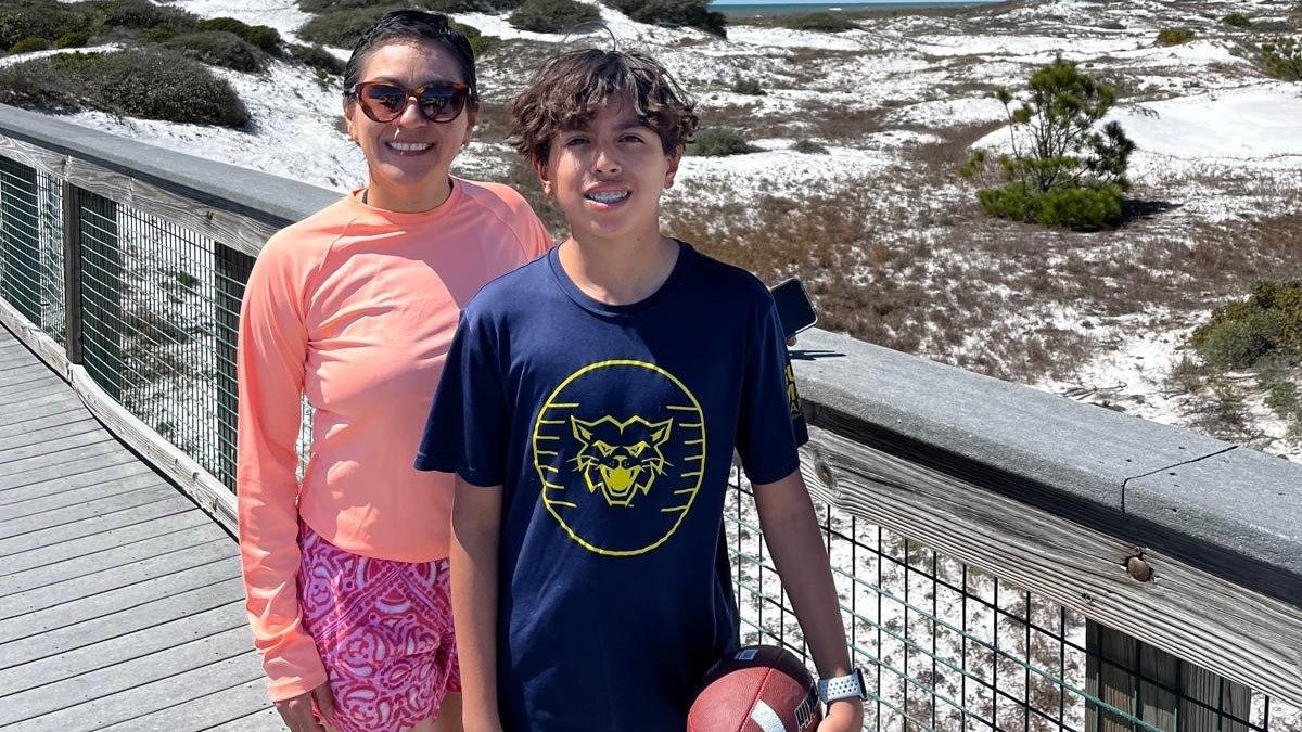Woman wearing a peach shirt stands next to a young boy holding a football
