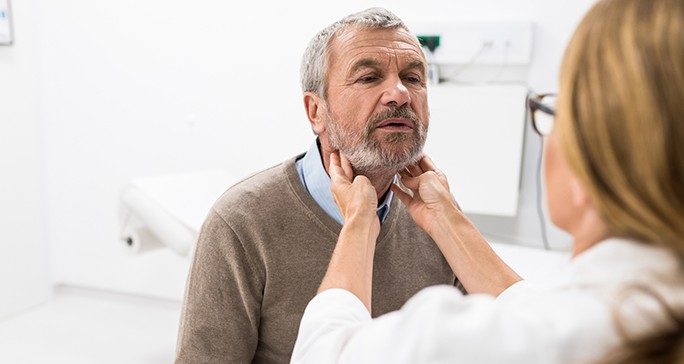 Female physician feels around the neck of an older male patient