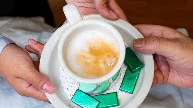 One person hands a latte on a plate surrounded by green mints to a person in bed.