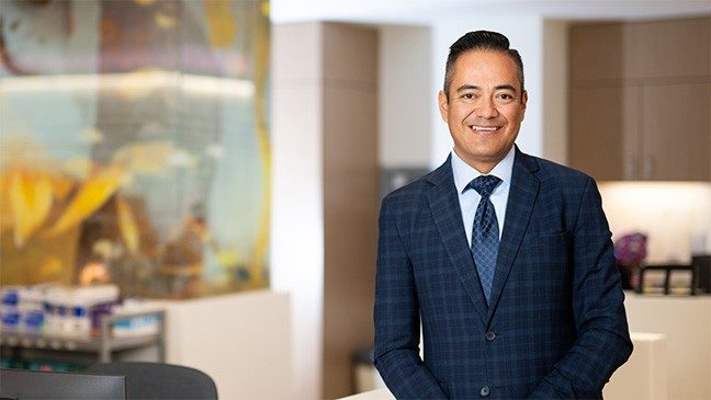 Man in navy plaid suit smiles in front of an aquarium